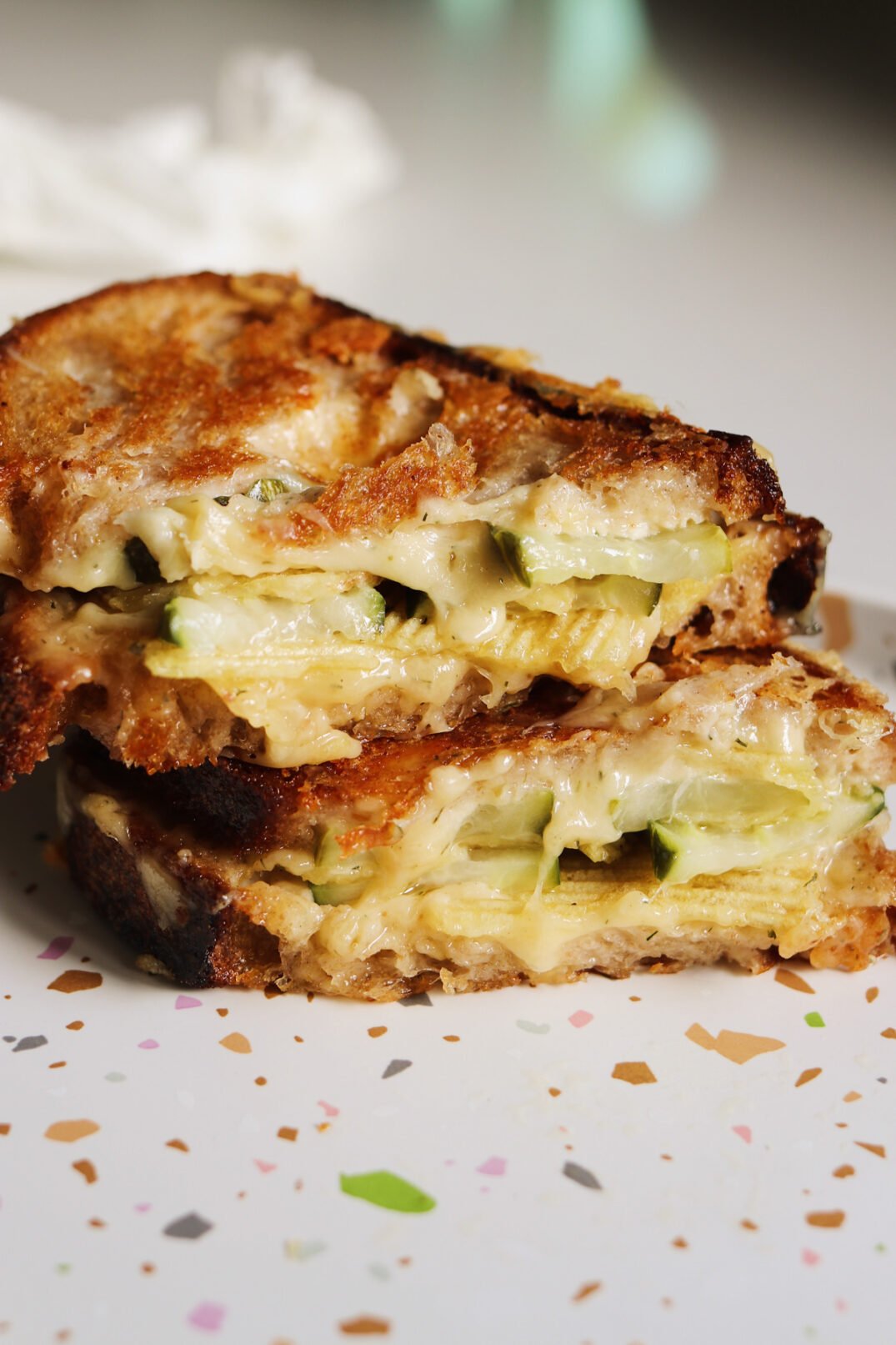 a dill pickle grilled cheese cut in half sitting on a speckled plate.