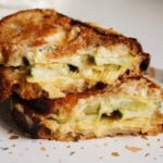 a dill pickle grilled cheese cut in half sitting on a speckled plate.