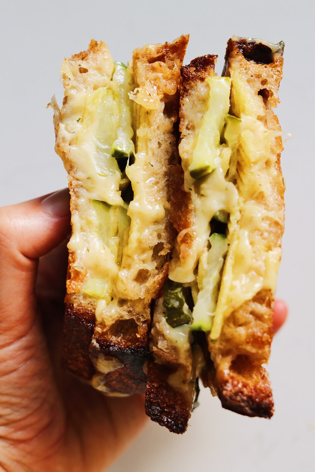 a hand holding two halves of a dill pickle grilled cheese.