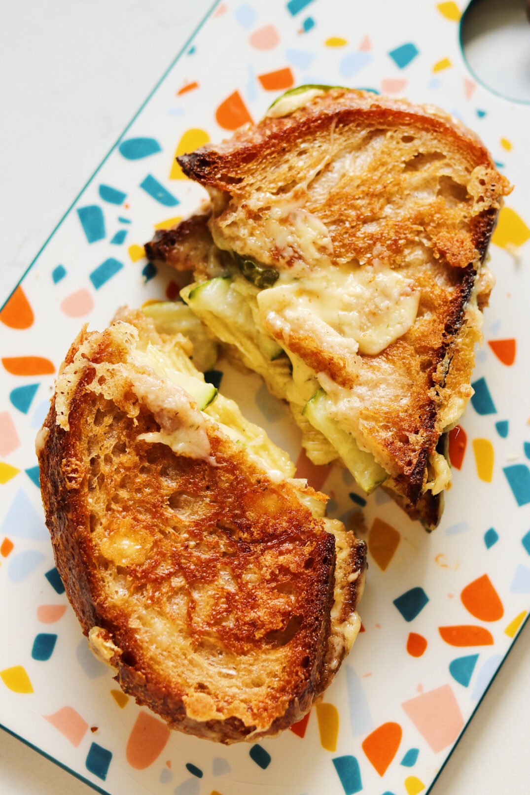 an overhead view of a dill pickle grilled cheese cut in half with cheese oozing out.