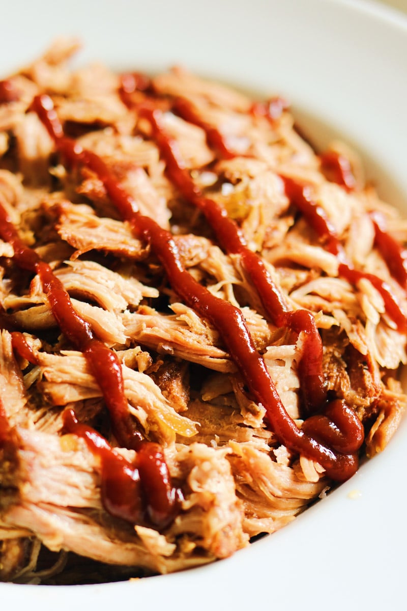 a bowl of dr pepper pulled pork with a drizzle of southern bbq sauce. 