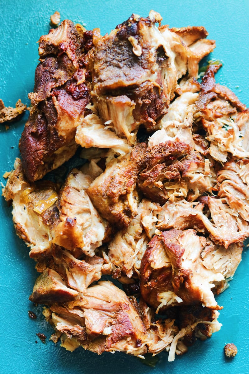 a pile of pulled pork on a teal cutting board. 