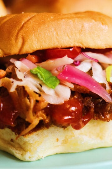 an up close view of a pulled pork slide with coleslaw, sauce and pickled red onions on hawaiian rolls.
