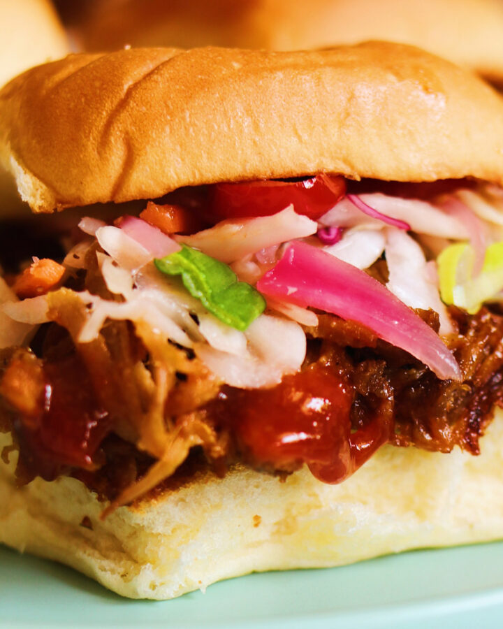 an up close view of a pulled pork slide with coleslaw, sauce and pickled red onions on hawaiian rolls.