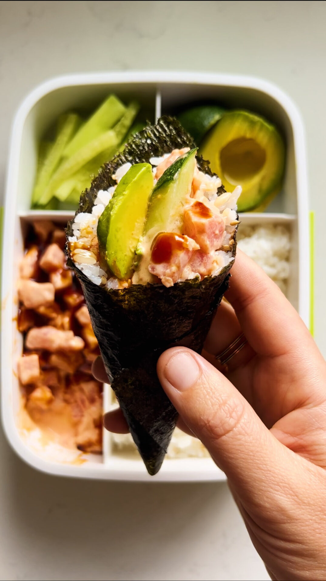 a hand hodling a spicy tuna hand roll sushi roll with avocado. 