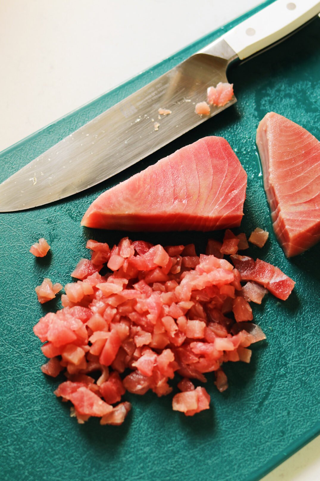 sashimi grade tuna on a cutting board being minced with a sharp knife. 