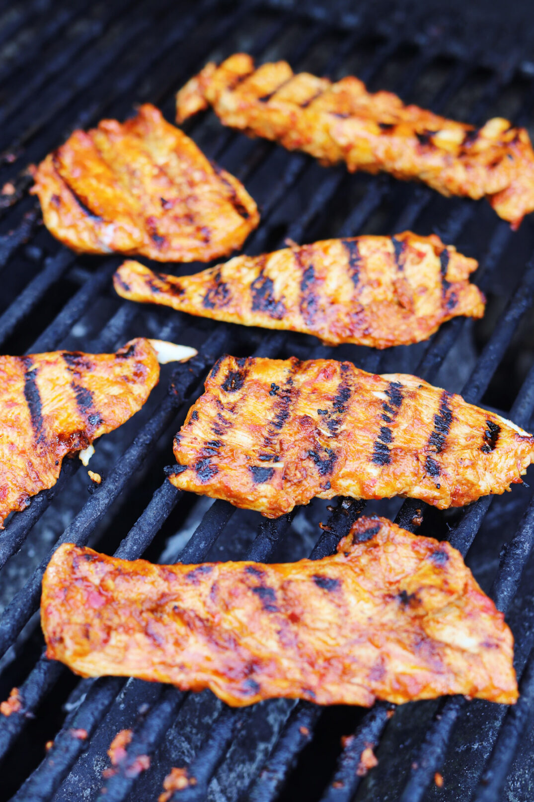 grill marked harissa chicken cooking on an outside grill. 