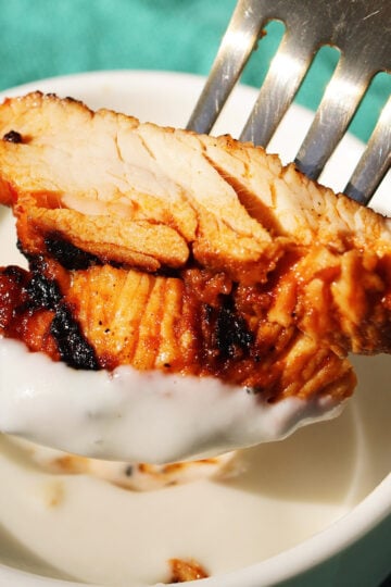 a fork holding a slice of harissa chicken dunking it into white garlic sauce.
