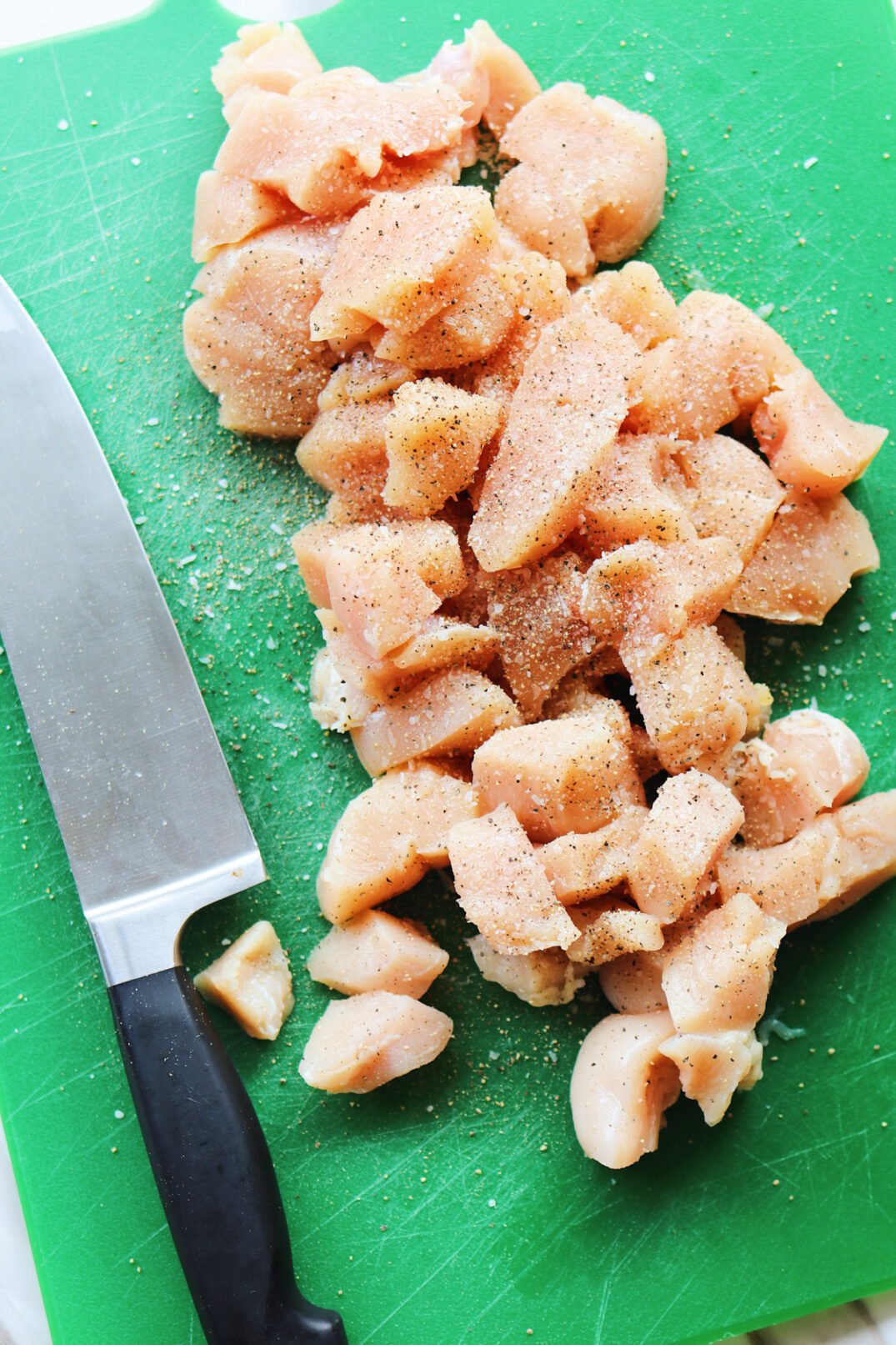 bite size chicken seasoned with salt and pepper on a cutting board with a knife. 
