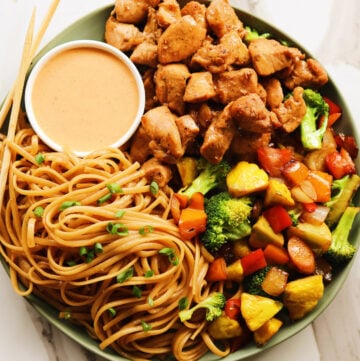 hibachi chicken with yum yum sauce on a green plate with vegetables and noodles.