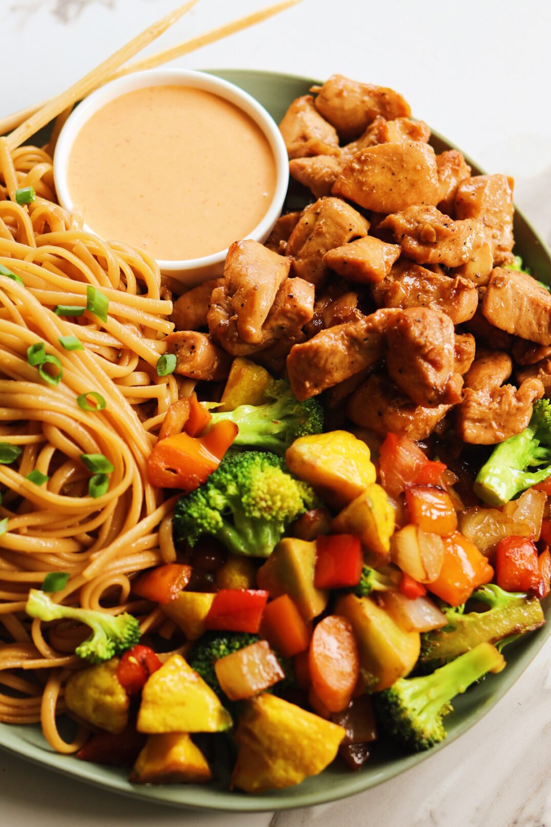 a plate of hibachi chicken with yum yum sauce, veggies and noodles on a white countertop. 
