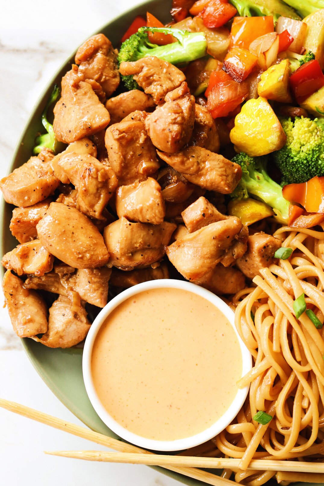 hibachi chicken with yum yum sauce on a plate with noodles and colorful vegetables. 