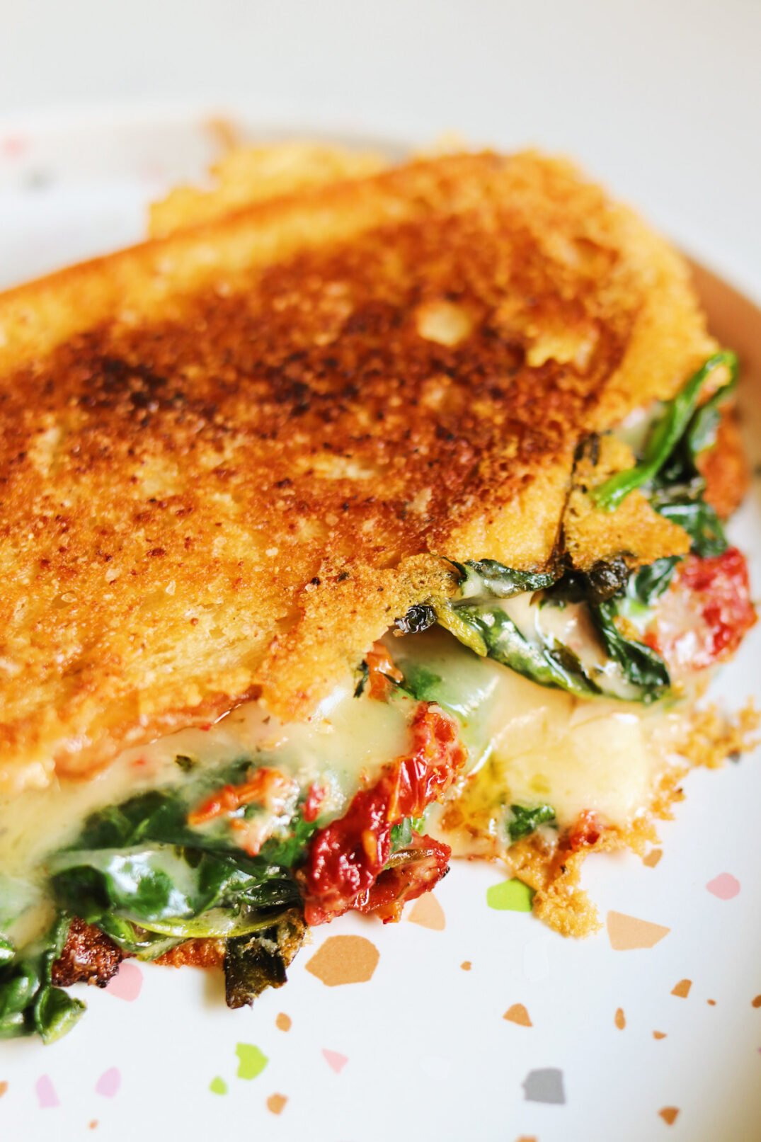 an up close view of the cheese oozing out of a grilled cheese with spinach and sun dried tomatoes. 