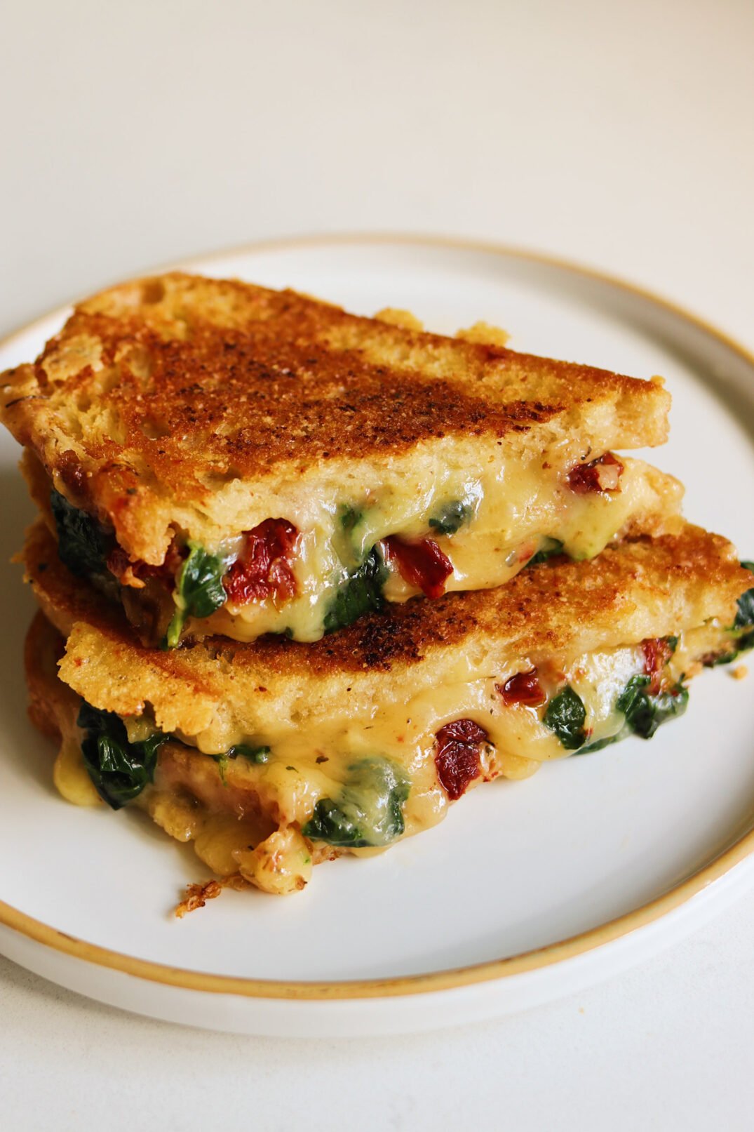 a grilled cheese on a plate with spinach and sun dried tomatoes