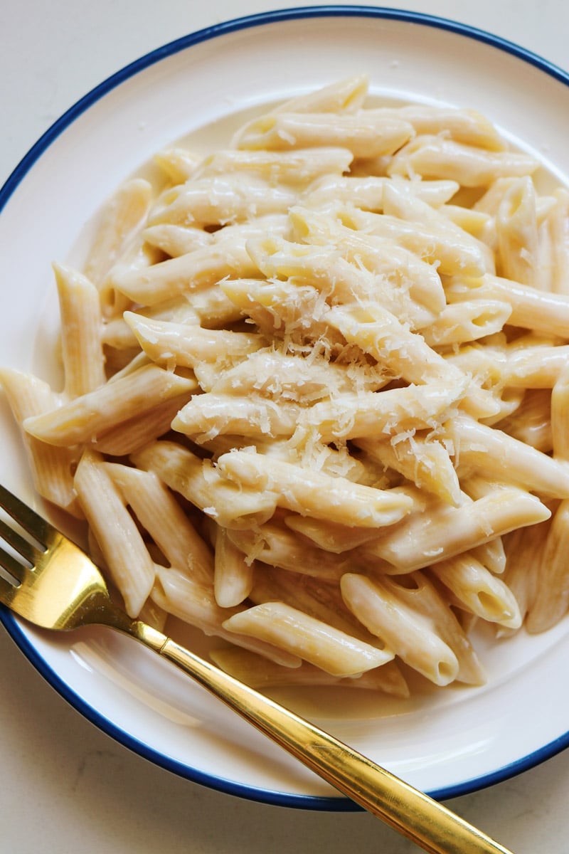a white bowl with a golden fork and a big serving of penne alfredo pasta. 
