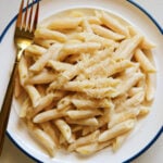 a white plate topped with a big serving of penne alfredo with creamy noodles.