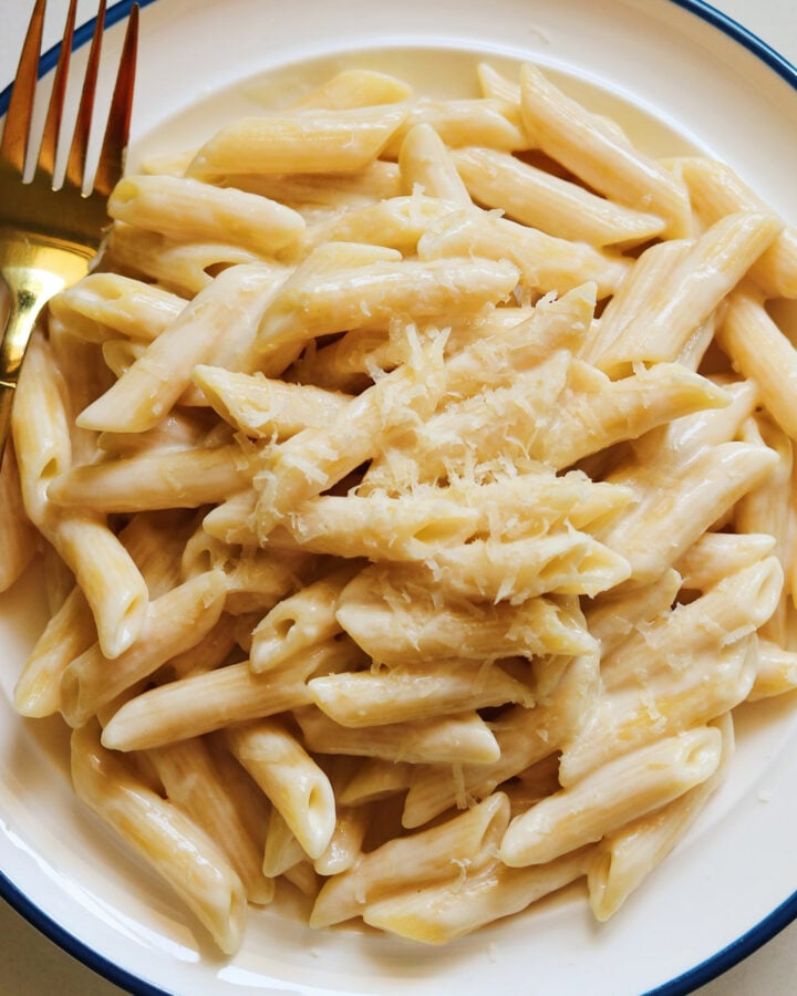 a white plate topped with a big serving of penne alfredo with creamy noodles.