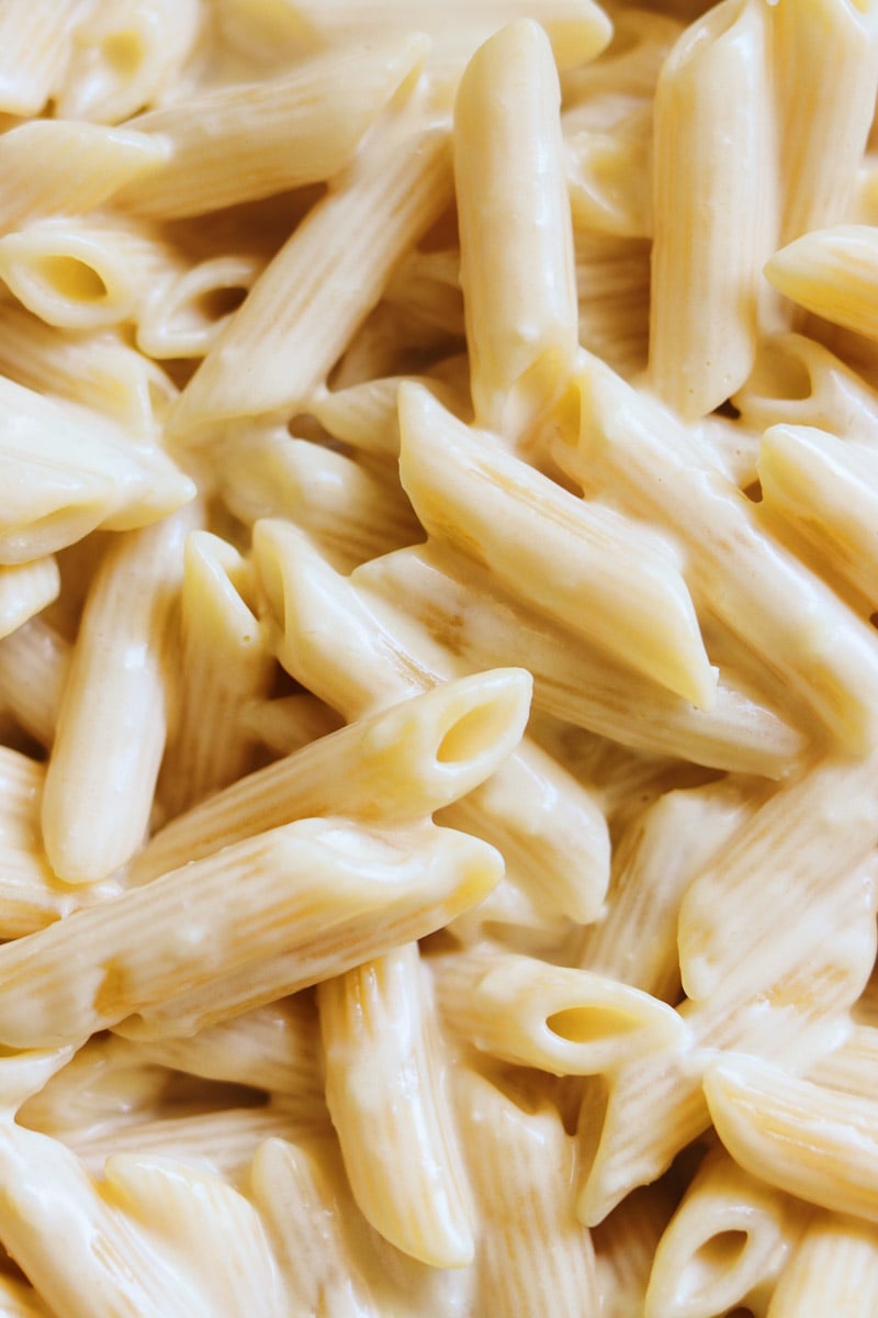 a close up view of the creamy noodles in a pot of penne alfredo. 