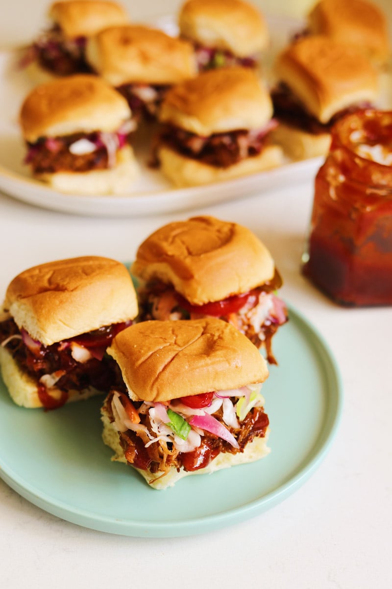 a plate of bbq pulled pork sliders with a jar of southern bbq sauce on the side. 