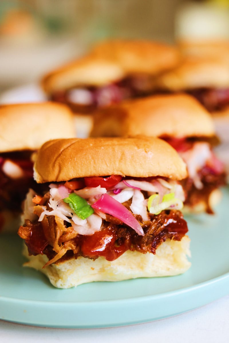 a tiny blue plate will colorful pulled pork sliders on it with a platter in the background.