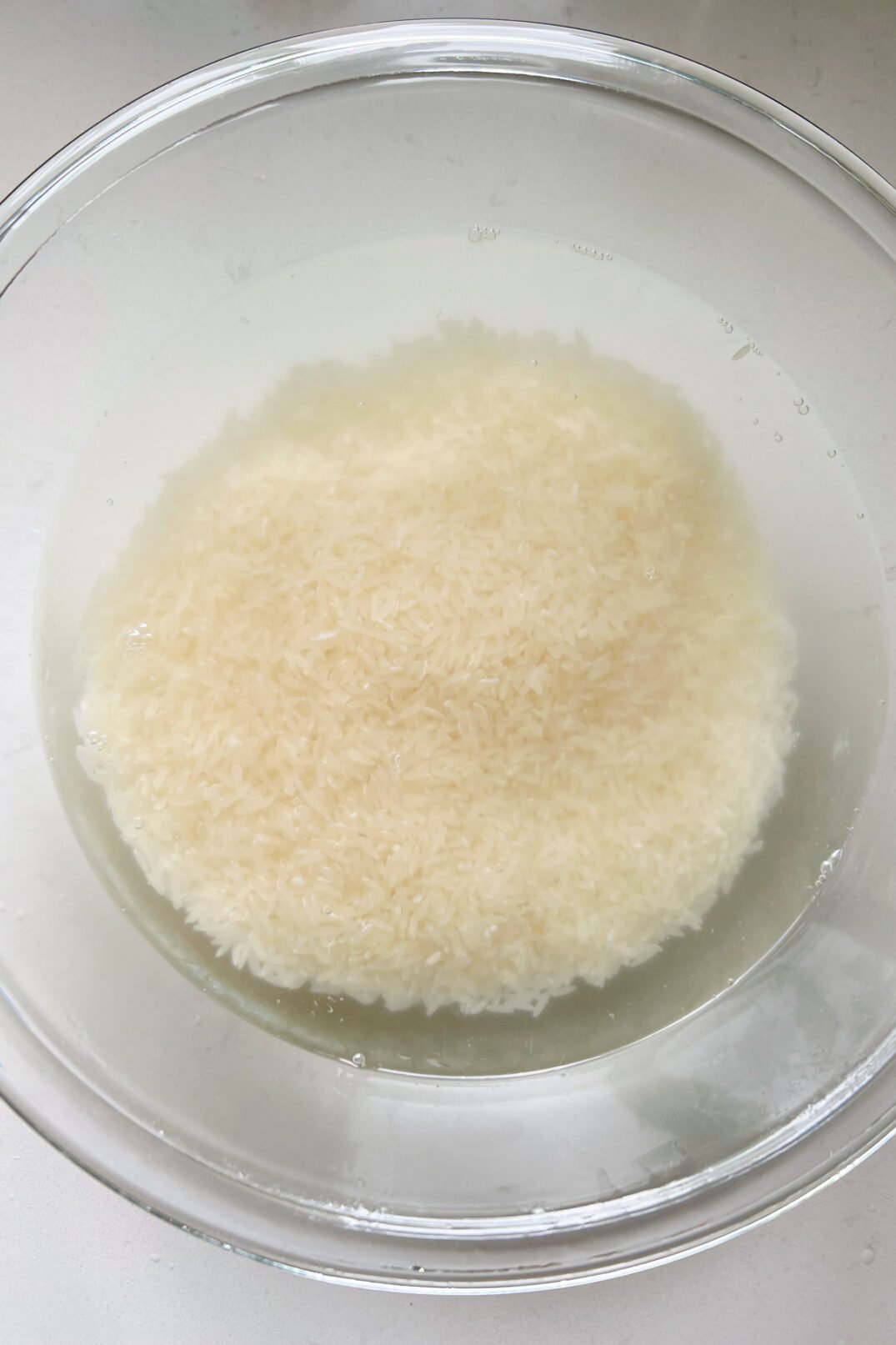 rice being rinsed in a glass bowl with clear water. 