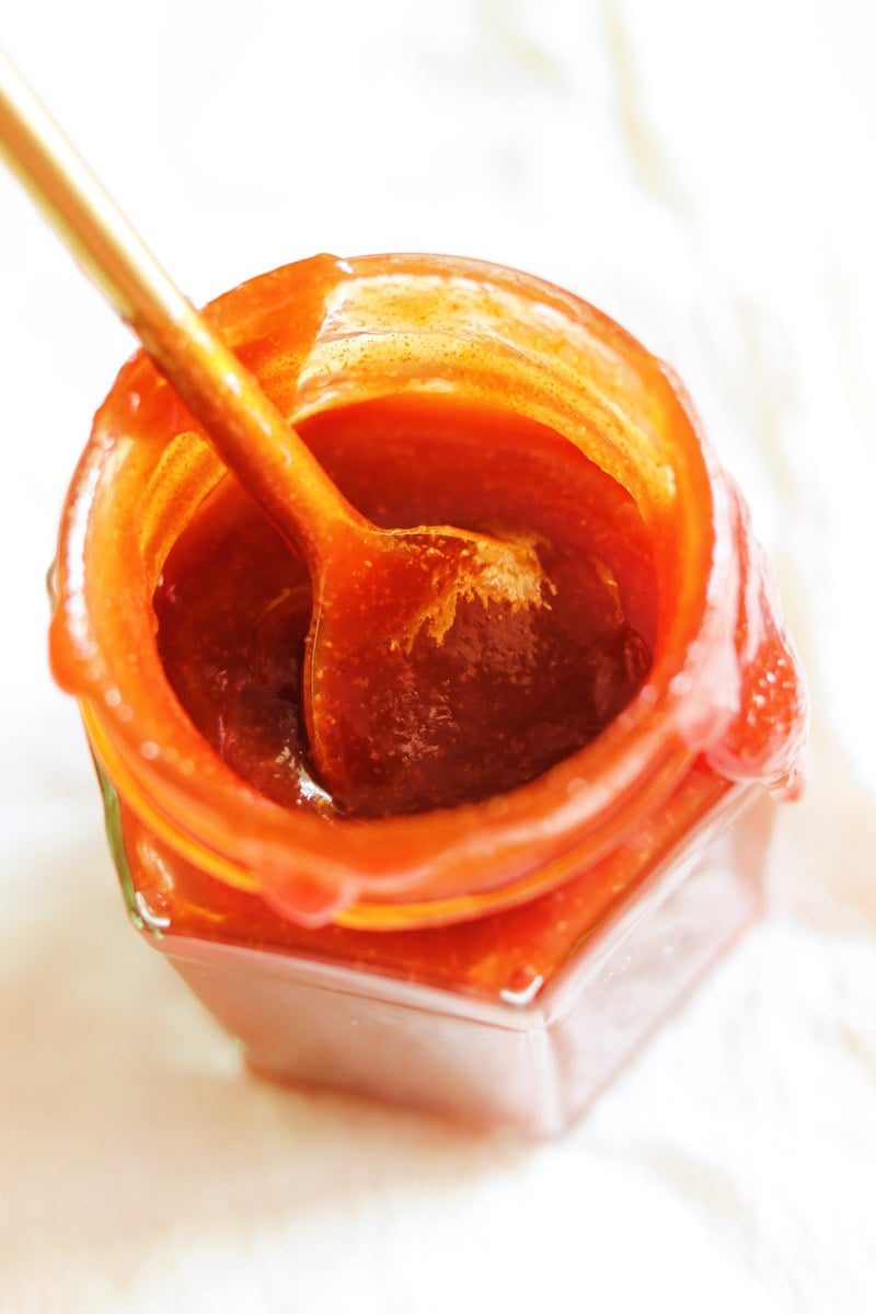 a spoon dunking into a jar of bbq sauce. 
