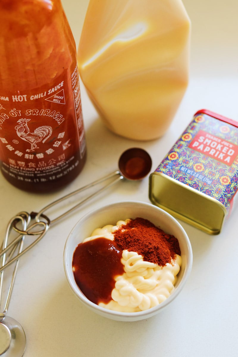 step 1 of making creamy sriracha sauce - all ingredients on a table with a small mixing bowl.