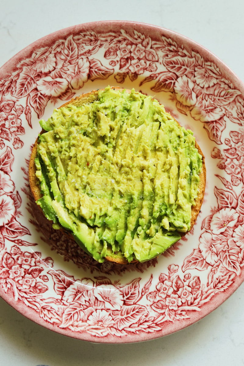 avocado mashed onto the bottom half of a toasted bagel. 
