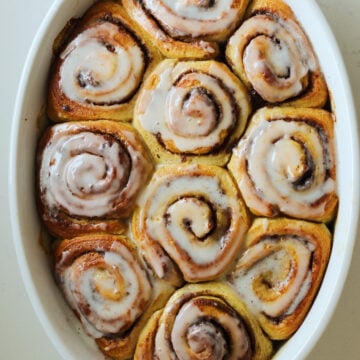 a batch of cinnamon rolls with heavy cream and icing in a white baking dish.