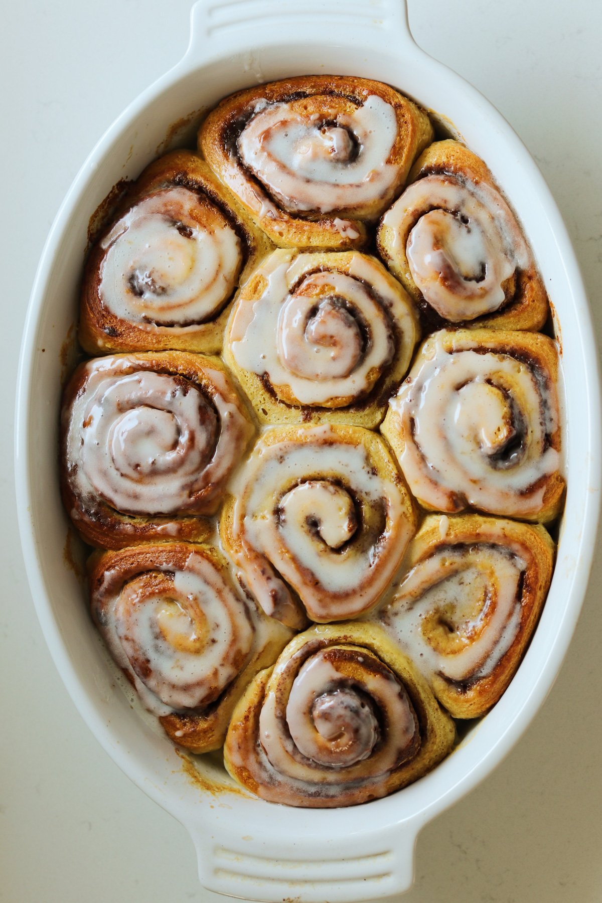 a batch of cinnamon rolls with heavy cream and icing in a white baking dish. 