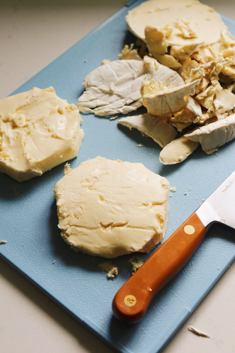 a picture of two wheels of brie with the rind cut off on a blue cutting board. 