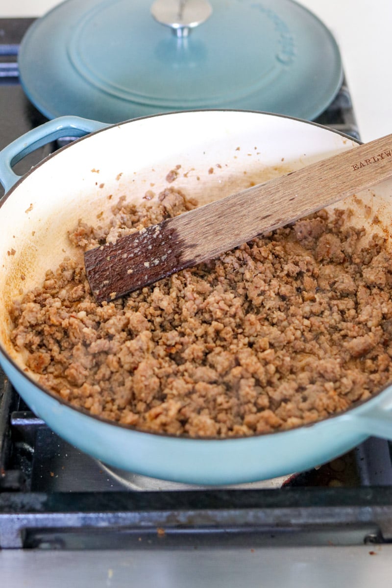 crumbled sausage being cooked in a blue braising dish. 