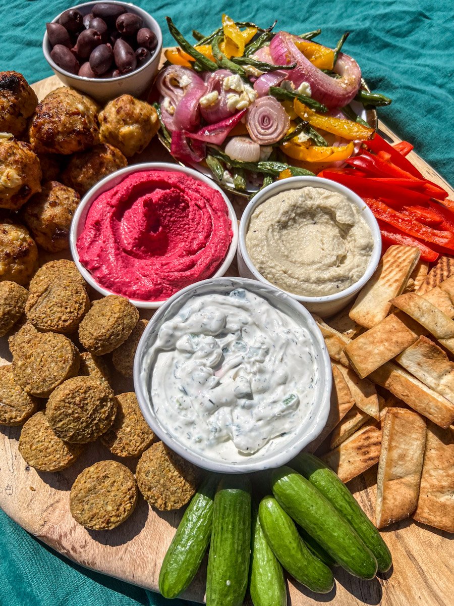a wooden board filled with colorful mediterranean appetizers and dips. 