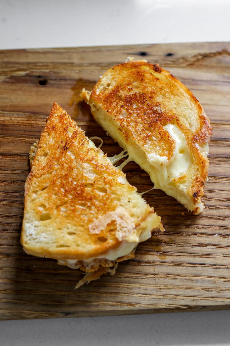 two halves of a garlic bread grilled cheese on a wooden cutting board with a cheese pull between the two. 