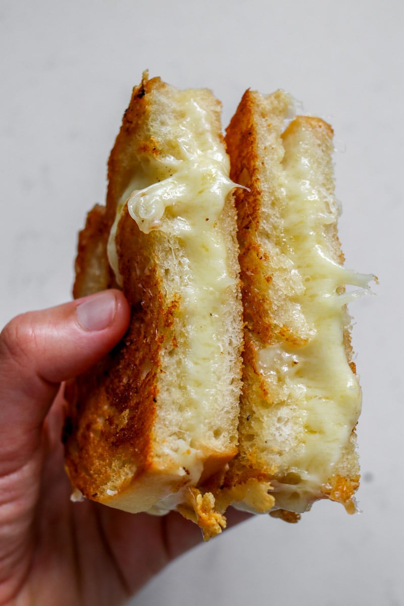 two hands holding two halves of a garlic bread grilled cheese with toum squeezing out. 