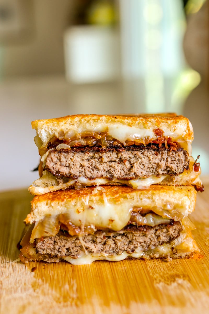 two halves of a patty melt with bacon and caramelized onions sitting on top of each other. 