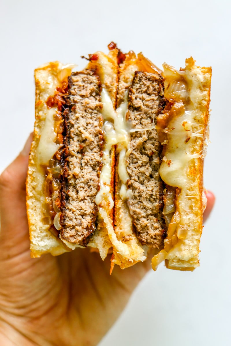a hand holding two halves of a bubba burger patty melt.