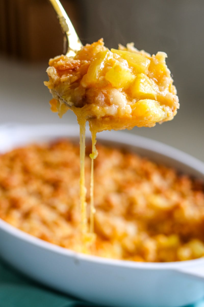 a cheese pull coming from a spoon full of cheesy pineapple casserole. 
