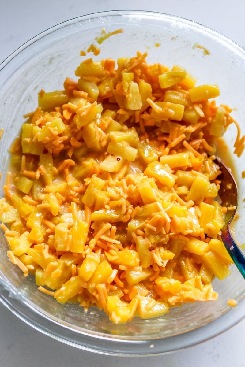 a glass bowl full of pineapple tidbits and cheddar cheese. 