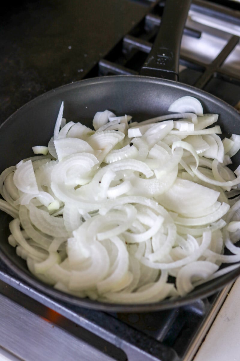 thinly sliced onions in a black pan on a stovetop. 