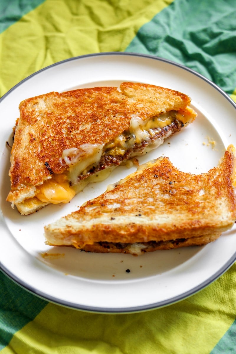 a smash burger grilled cheese sitting on a white plate with a green background. 