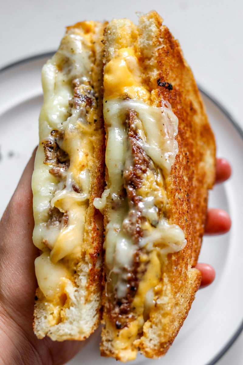 a hand holding two halves of a smashburger grilled cheese