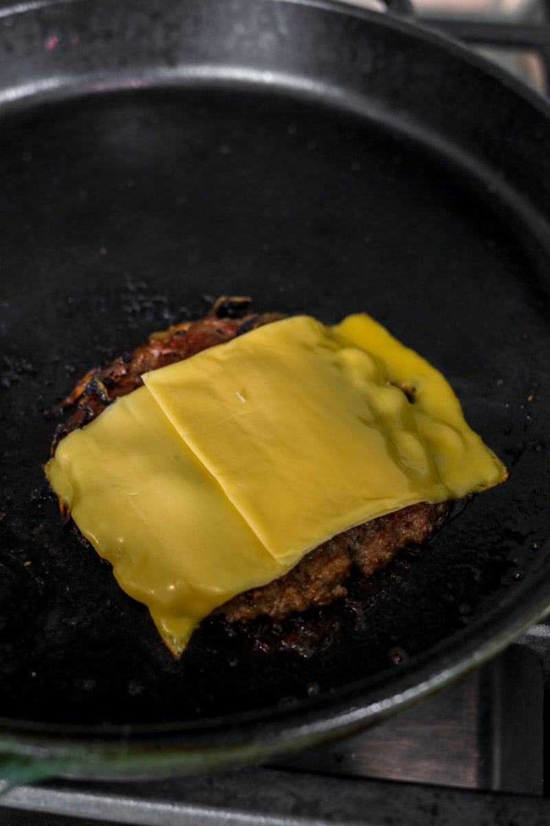 a smashburger on the grill topped with two slices of american cheese. 