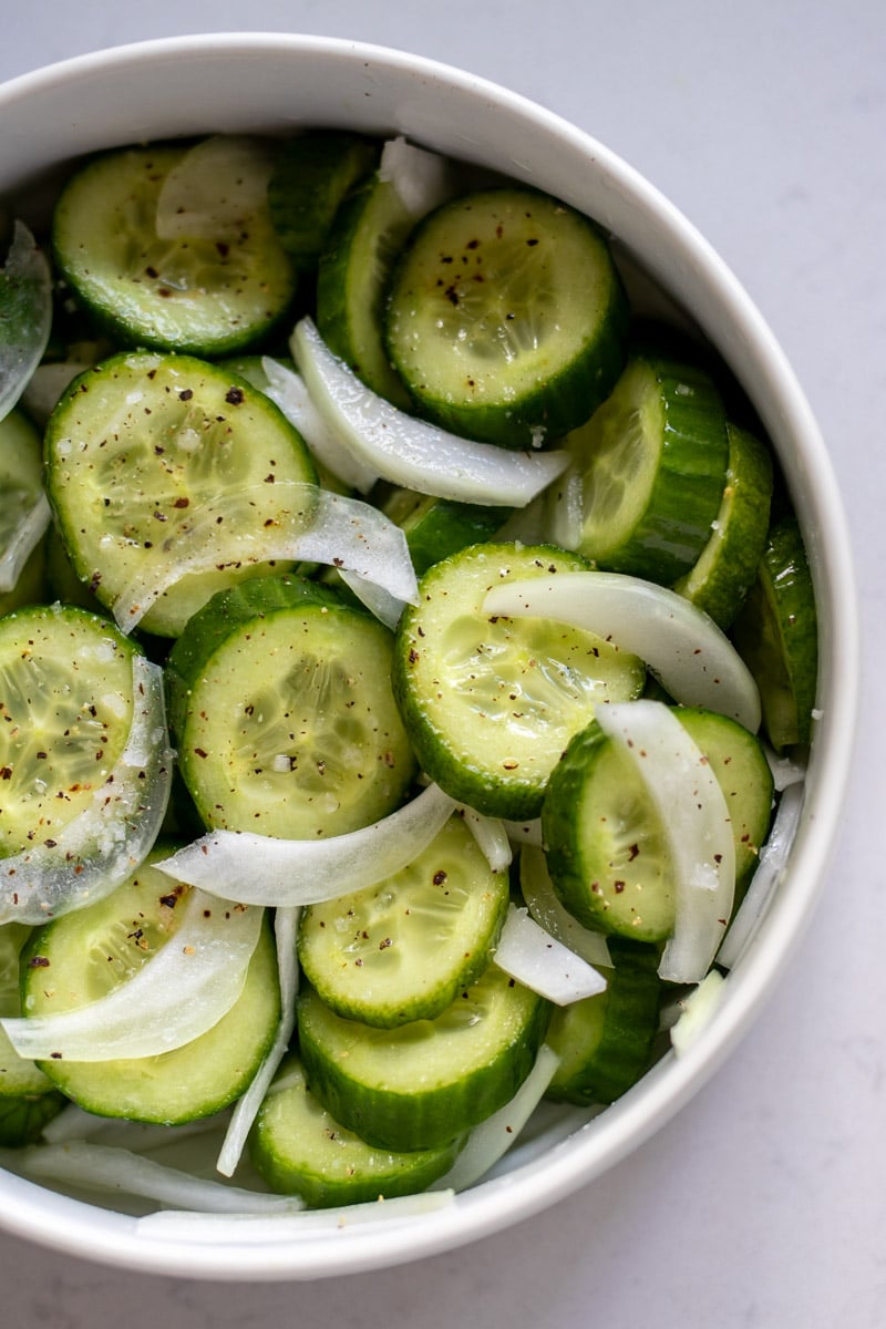 the right side of a white bowl of cucumber salad with thinly sliced onions, vinegar and sugar.