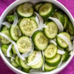 cucumber salad with sliced onions, salt, pepper in a white bowl with a pink background.