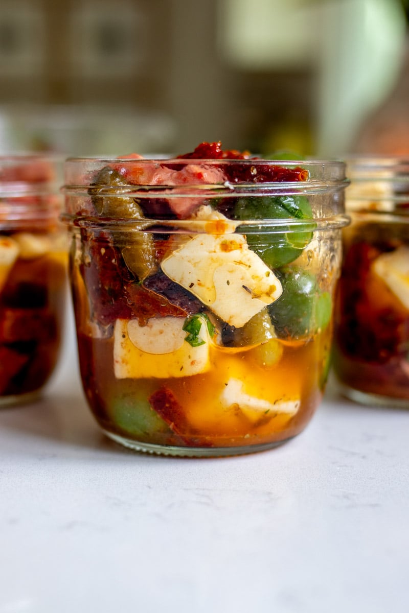 glass jars full of marinated cheese and colorful pickles.