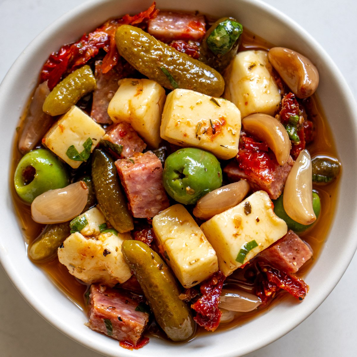 a white bowl full of marinated cheese and salami.