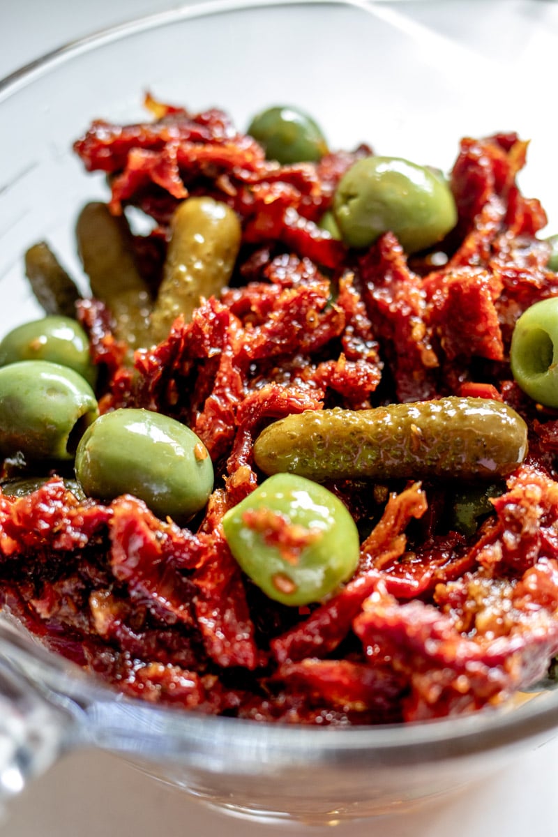 sun dried tomatoes, olives, and pickles in a glass bowl.