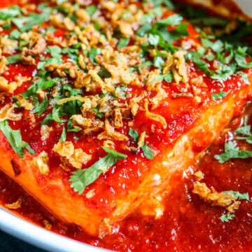 an overhead view of a spicy salmon recipe in a baking dish with bright red sauce on top.