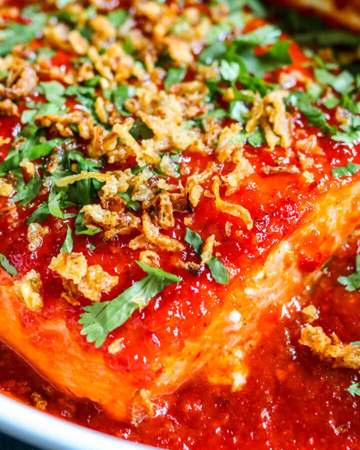 an overhead view of a spicy salmon recipe in a baking dish with bright red sauce on top.